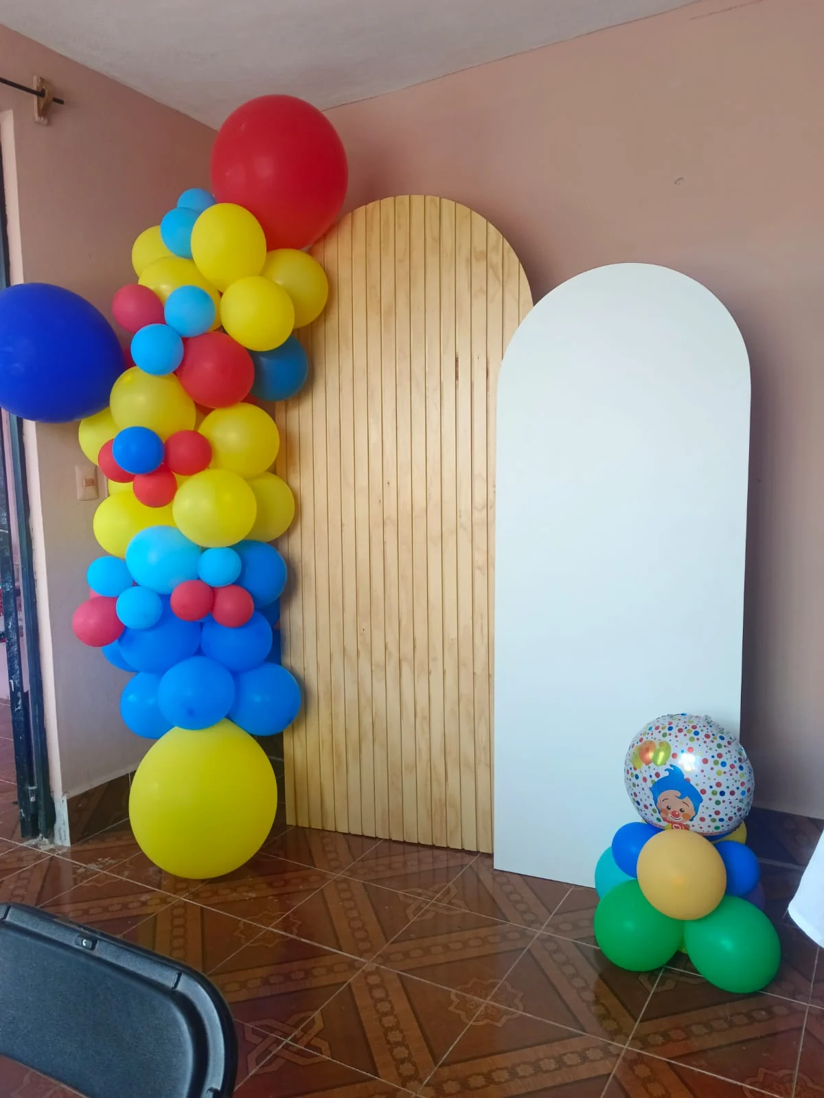 Montaje previo con arco de globos multicolor, panel de madera y panel blanco